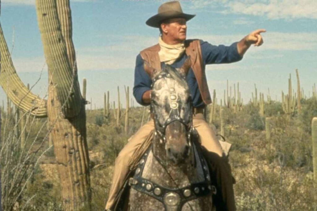 John Wayne a cavallo in una scena di un film western