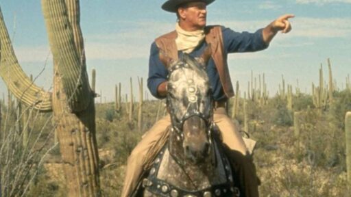 John Wayne a cavallo in una scena di un film western